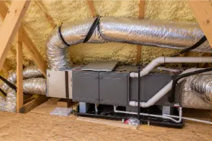 HVAC air handling unit with insulated silver ductwork and PVC condensate pipes installed in a spray-foam-insulated attic.