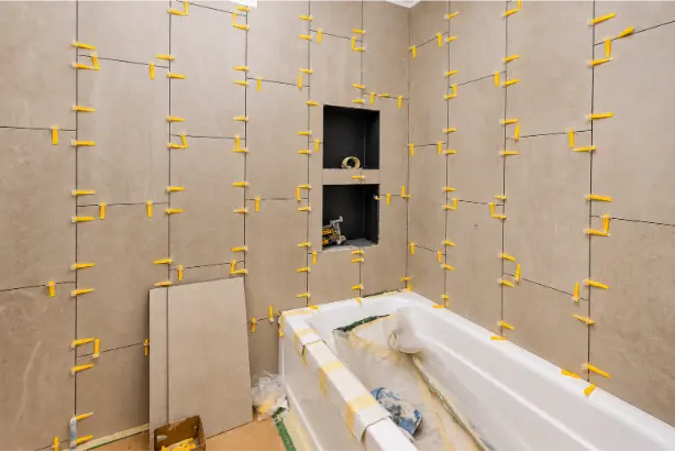 Bathroom renovation in progress with beige wall tiles, yellow tile levelling clips, recessed wall niches and a protected white bathtub.