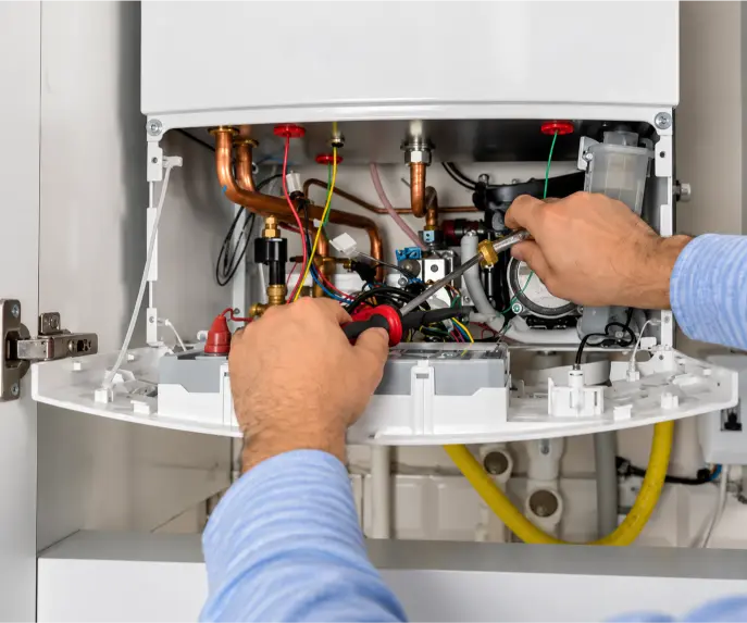 Technician servicing an open wall-mounted boiler, adjusting internal brass fittings and components with hand tools.