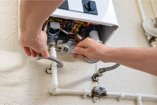 Plumber repairing a wall-mounted boiler using an adjustable wrench on a pipe fitting with flexible braided hoses.