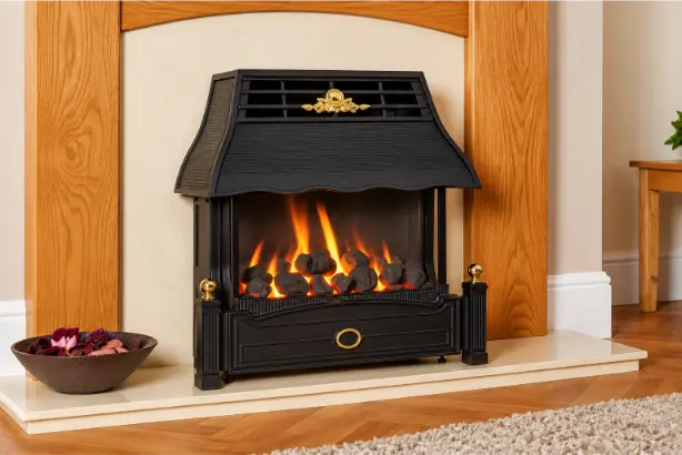 Classic black gas fireplace with glowing flames, gold accents, and oak wood mantel in a cozy living room.