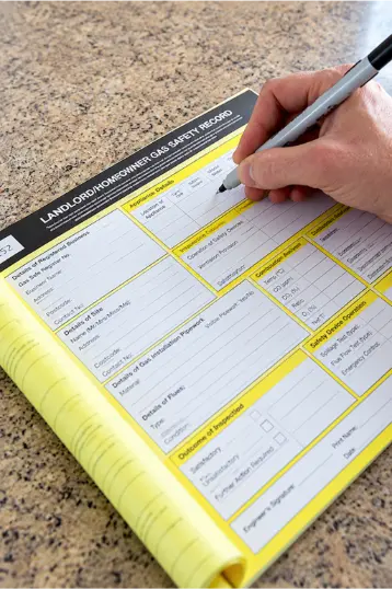 Hand completing a landlord gas safety record form during a gas safety inspection.