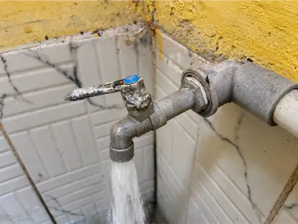 Close-up of a corroded outdoor tap leaking water against a stained tiled wall