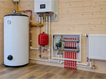 Domestic heating system with hot water cylinder, wall-mounted boiler, red expansion vessel, underfloor heating manifold, copper pipework and white radiator.