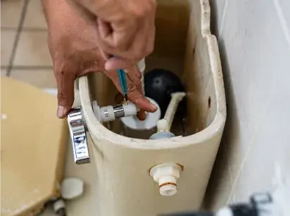 Plumber repairing a toilet cistern flush mechanism with a screwdriver